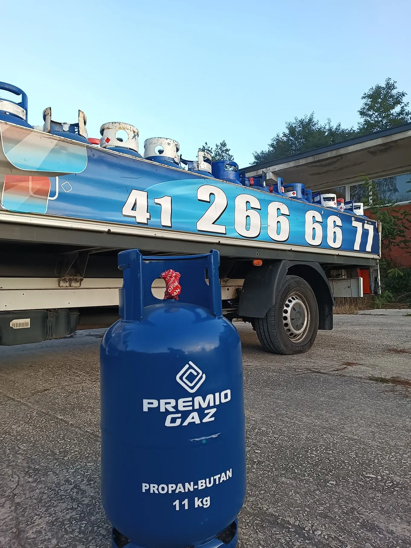 Butla z gazem z logo firmy PremioGaz na tle samochodu dostawczego.